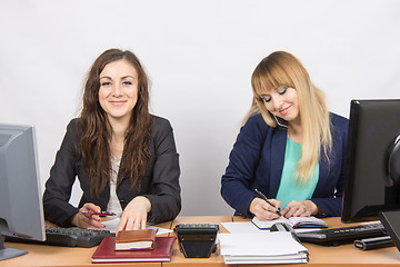 Image showing  Young girls in the office, one looks in the frame, the second talking on the phone and writing in diary