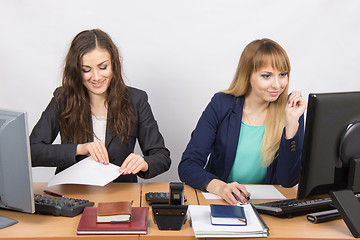 Image showing Two young women working in the office, one of fun took a sheet of paper, the second looks at the computer screen