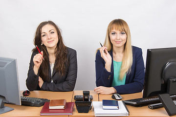 Image showing Two business women sitting at a desk, holding pen in hand and look to the Frame