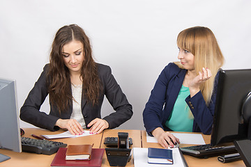 Image showing Two young girls working in an office, making a paper airplane, and the second with hatred looks at her