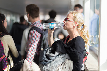 Image showing  Woman drinking water while queuing to board plane.