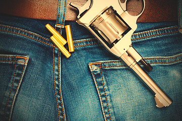 Image showing silvery revolver with cartridges on old blue jeans