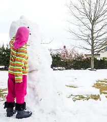 Image showing Girl making snowman in garden, hiding under pink hat