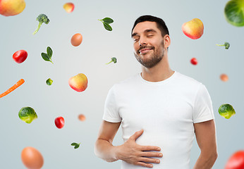 Image showing happy full man touching tummy over falling fruits