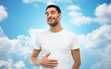 Image showing happy full man touching tummy over blue sky