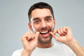 Image showing man with dental floss cleaning teeth over gray