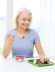 Image showing smiling woman eating fruits with tablet pc at home