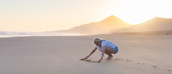 Image showing Lady drawing heart shape in sand on beach.