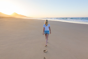 Image showing Lady walking on sandy beach in sunset leaving footprints behind.