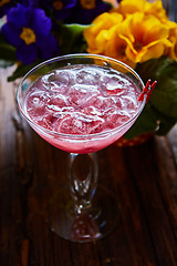 Image showing cosmopolitan cocktail garnished with ice on wooden table 