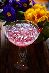 Image showing cosmopolitan cocktail garnished with ice on wooden table 