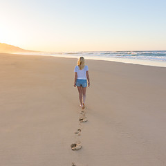 Image showing Lady walking on sandy beach in sunset leaving footprints behind.