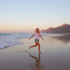 Image showing Lady enjoying running from waves on sandy beach in sunset.