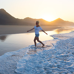 Image showing Lady enjoying running from waves on sandy beach in sunset.