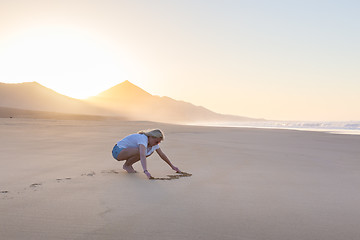 Image showing Lady drawing heart shape in sand on beach.