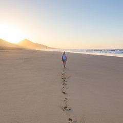 Image showing Lady walking on sandy beach in sunset leaving footprints behind.
