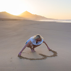 Image showing Lady drawing heart shape in sand on beach.