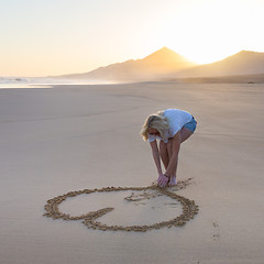 Image showing Lady drawing heart shape in sand on beach.