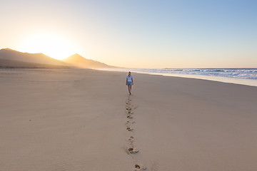 Image showing Lady walking on sandy beach in sunset leaving footprints behind.