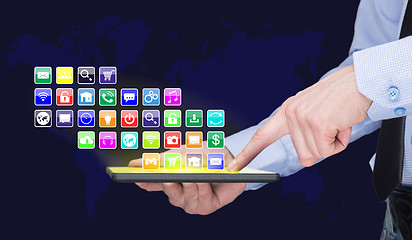 Image showing Businessman holding a tablet pc with mobile applications icons on virtual screen . Internet and business concept. World map