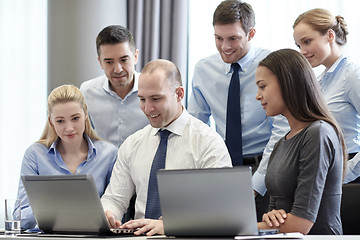 Image showing smiling businesspeople with laptops in office