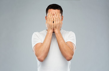 Image showing man in white t-shirt covering his face with hands