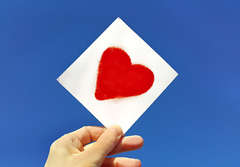 Image showing Hand holding a picture of a heart against the blue sky