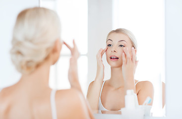 Image showing happy woman applying cream to face at bathroom