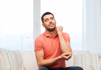 Image showing unhappy man suffering from pain in hand at home