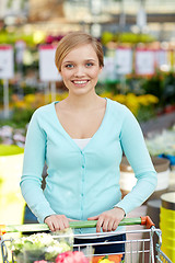 Image showing happy woman with shopping cart and flowers in shop