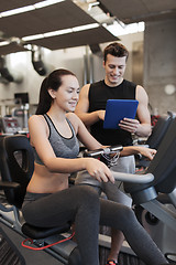 Image showing happy woman with trainer on exercise bike in gym