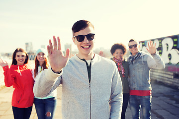 Image showing happy teenage friends waving hands on city street