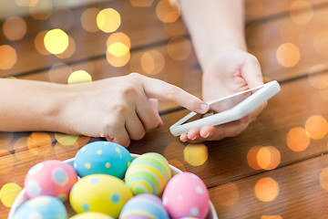 Image showing close up of hands with easter eggs and smartphone