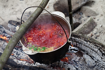 Image showing Borscht cooking in sooty cauldron on campfire