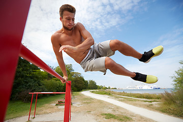 Image showing young man exercising on horizontal bar outdoors