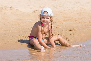 Image showing Five-year girl in a cap sits on the sand on beach