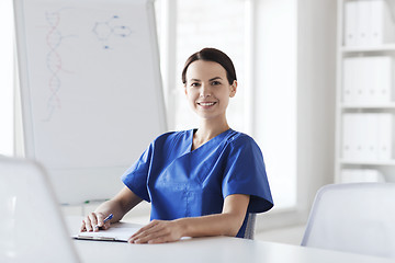 Image showing happy female doctor or nurse writing to clipboard