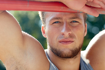 Image showing young man exercising on horizontal bar outdoors