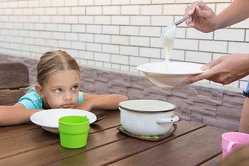 Image showing Upset six-year girl dissatisfied looks at his mother who puts porridge for breakfast