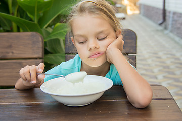 Image showing Upset six year old girl looking sadly at the semolina in a spoon at breakfast