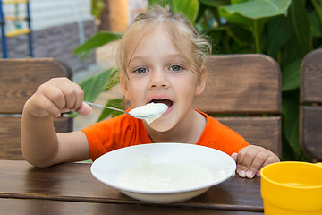 Image showing Funny five-year girl with pleasure eats porridge for breakfast