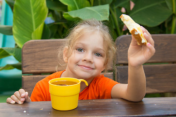 Image showing  Girl smiling and eating a sandwich with tea for breakfast