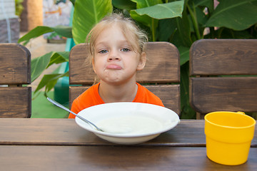 Image showing Upset five year old girl poses faces unwilling to eat porridge for breakfast