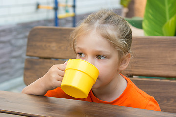 Image showing Four-year-girl drinking a drink sitting at the table on the veranda