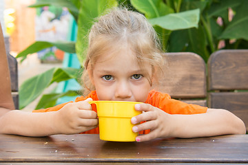 Image showing Four-year girl drinks a drink from the cup and looks in the frame