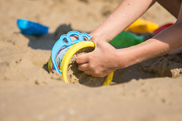 Image showing The baby is gaining a bucket in the wet sand, close-up