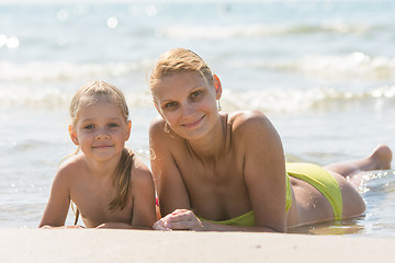 Image showing Mom and daughter are in the four-year water on the sandy seafront and joyfully look to the Frame