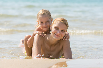 Image showing Young woman with a daughter on his back lying on the beach and smiling