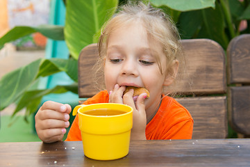 Image showing Four-year girl funny stuffed bun in his mouth and looks at a glass of tea