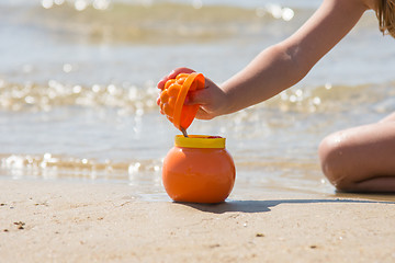 Image showing Child sprinkles wet sand from the molds in a pot on the sandy beach seashore